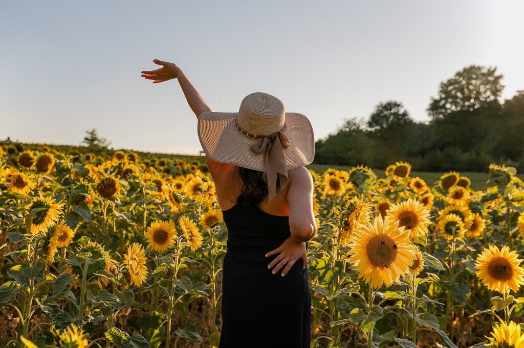 Is Financial freedom Legit? A lady wearing a black dress and a brown hat, chasing her love for sunflowers as against money during summer.