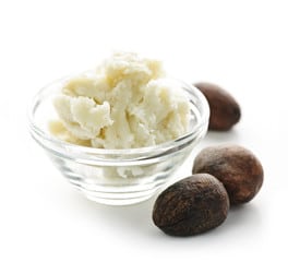 African Raw Shea butter in a transparent bowl with three shea nuts on the side.