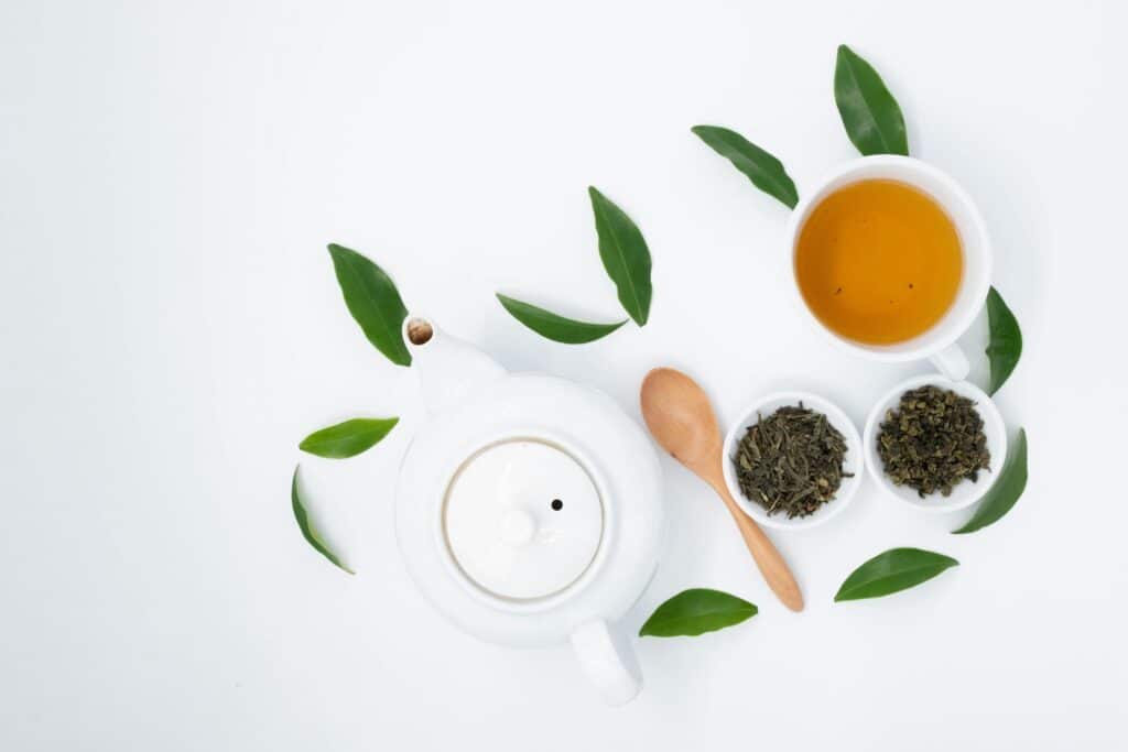 Green tea in two white jars served in a white jug and a cup.