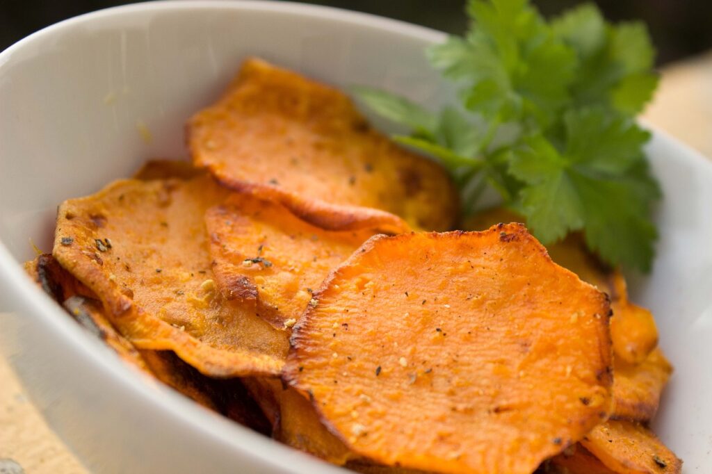 Sweet potato chips in a white bowl with little leaves on the side. Are sweet potatoes gluten free? Suitable for all.