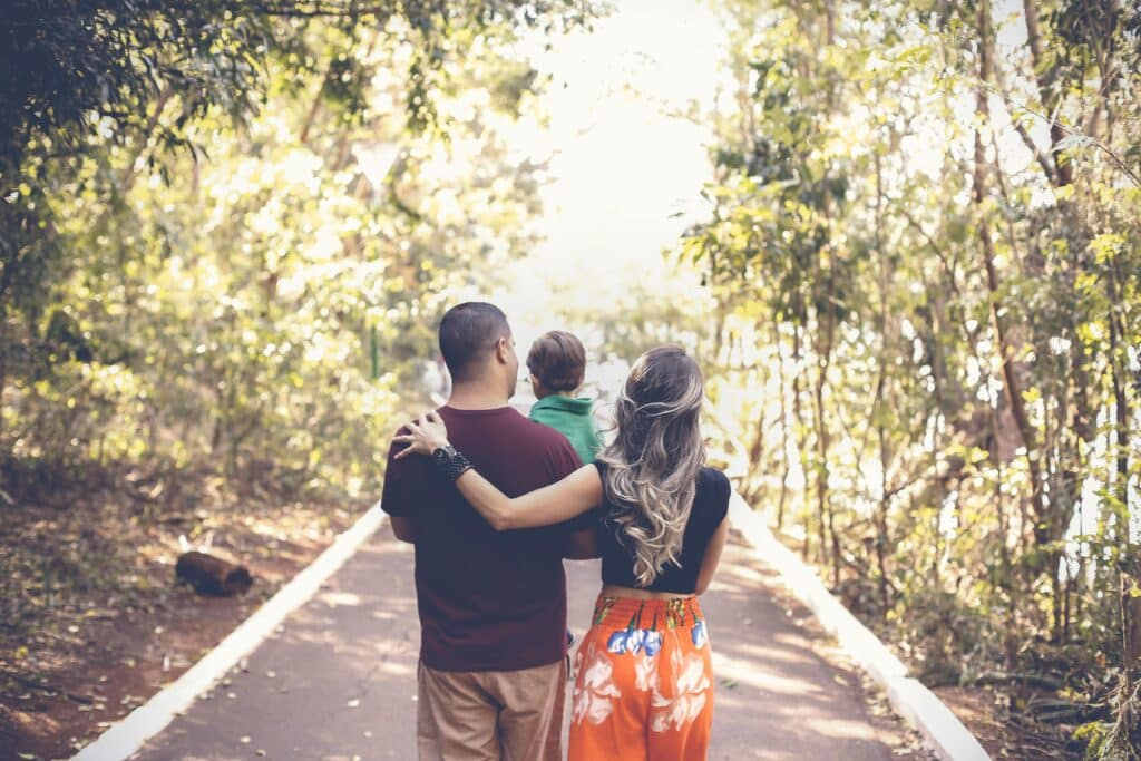 A family comprising of a man, a woman and baby taking a walk and chatting along.