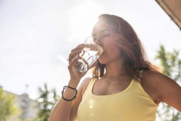 Dehydrated woman drinks clean warm or hot water from a glass to replenish fluids during hot summer days